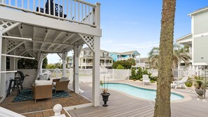 A covered outdoor area with a pool, wicker furniture, and a white fence. - Beach Retreat with Pool and Fire Pit (Holden Beach)