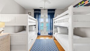 A room with bunk beds, a ceiling fan, and a view of a house through the door. - Beach Retreat with Pool and Fire Pit (Holden Beach)