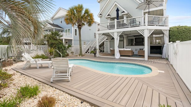 A two-story house with a swimming pool, outdoor furniture, and a covered deck area. - Beach Retreat with Pool and Fire Pit (Holden Beach)