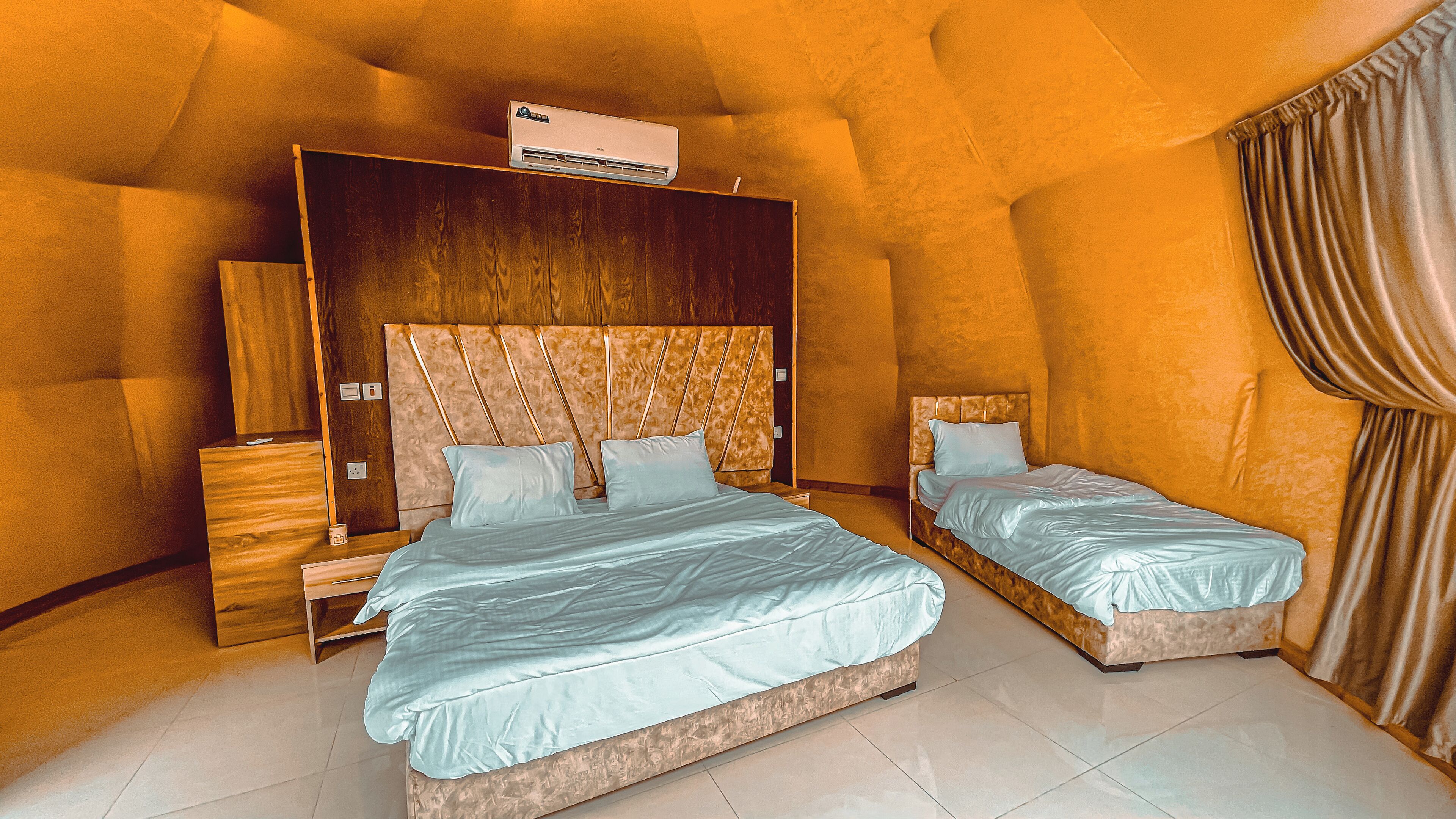 A bedroom with two beds, a wooden headboard, an air conditioning unit, and a nightstand.