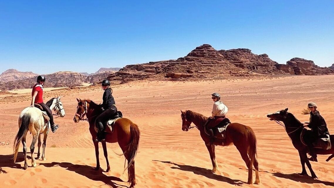 Un groupe de personnes à cheval, évoluant dans un paysage désertique, avec des formations rocheuses en arrière-plan.