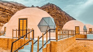 A row of dome-shaped tents with wooden railings and steps leading up to them, set against a mountainous backdrop.