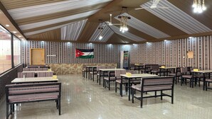 A restaurant with a high ceiling, patterned walls, and a flag. Tables and chairs are arranged for dining.