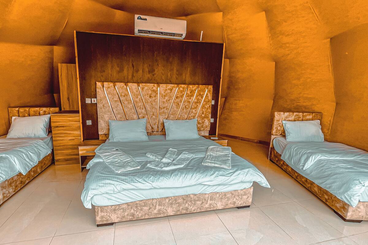 A bedroom with a large bed, two smaller beds, wooden headboards, and an air conditioning unit.