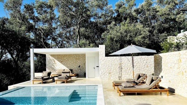 Un área de piscina moderna al aire libre con sillones de descanso y un muro de piedra de fondo.