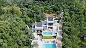 Una villa moderna con piscina, rodeada de abundante vegetación y colinas.