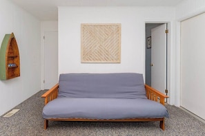 Een kamer met een enkel bed, een houten hoofdbord, een decoratief paneel aan de muur, en een deur naar een andere kamer.