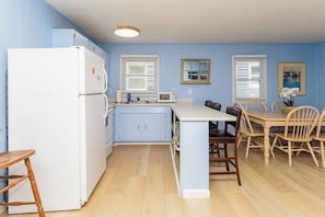 Een kleine keuken met een koelkast, magnetron en een houten eettafel met stoelen.
