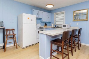 A kitchen with a white refrigerator, stove, and microwave. There are wooden chairs and a small island with a white countertop. - Midtown OC Unit 2, Oceanblock / Sleeps 8 (Ocean City)