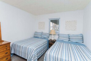 A bedroom with two single beds, a wooden dresser, a nightstand with a lamp, and decorative wall art. - Midtown OC Unit 2, Oceanblock / Sleeps 8 (Ocean City)