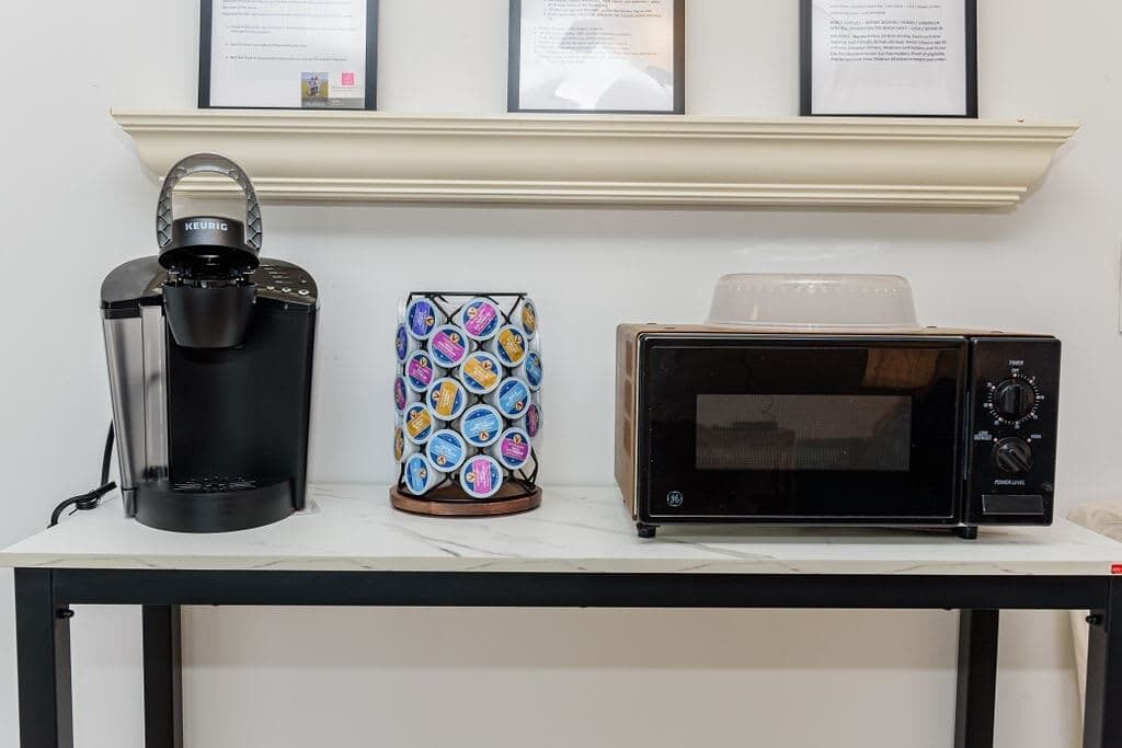 A table with a Keurig coffee maker, a colorful coffee pod holder, and a microwave oven.
