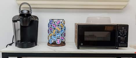 A table with a Keurig coffee maker, a colorful coffee pod holder, and a microwave oven.