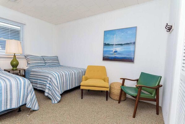 Une pièce avec deux lits, un fauteuil vert, un fauteuil jaune, une lampe et un tableau au mur.