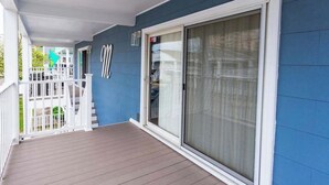 A covered porch with a wooden deck, a white railing, and a sliding glass door. - Midtown OC Unit 4/ Oceanblock / Sleeps 8 (Ocean City)