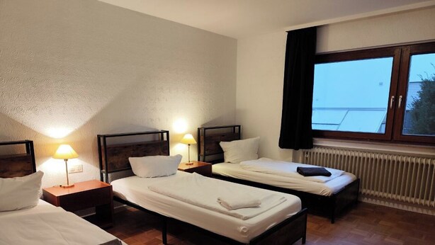 A hotel room with two single beds, wooden floors, a large window with curtains, and a radiator. - Completely Renovated House From 22 Euro pp and day (Baden-Baden)