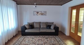 Una sala de estar con un sofá, un tapete estampado, un ventilador de techo y un cuadro en la pared.