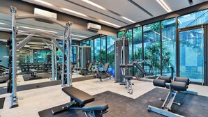Une salle de sport moderne équipée de divers appareils d’exercice, dotée de grandes fenêtres et offrant une vue sur la verdure environnante.