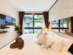 A hotel room with a bed, a TV, a window with curtains, and a view of buildings outside.