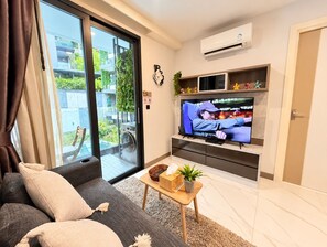 A modern living room with a sofa, a television, and a sliding glass door leading to a balcony.