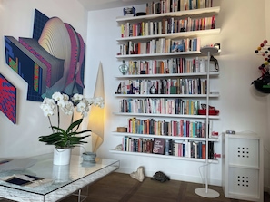 A room with a large bookshelf filled with books, a glass table with a plant, and abstract art on the wall. - Rome Historic Center, near famed Piazza del Popolo (Rome)