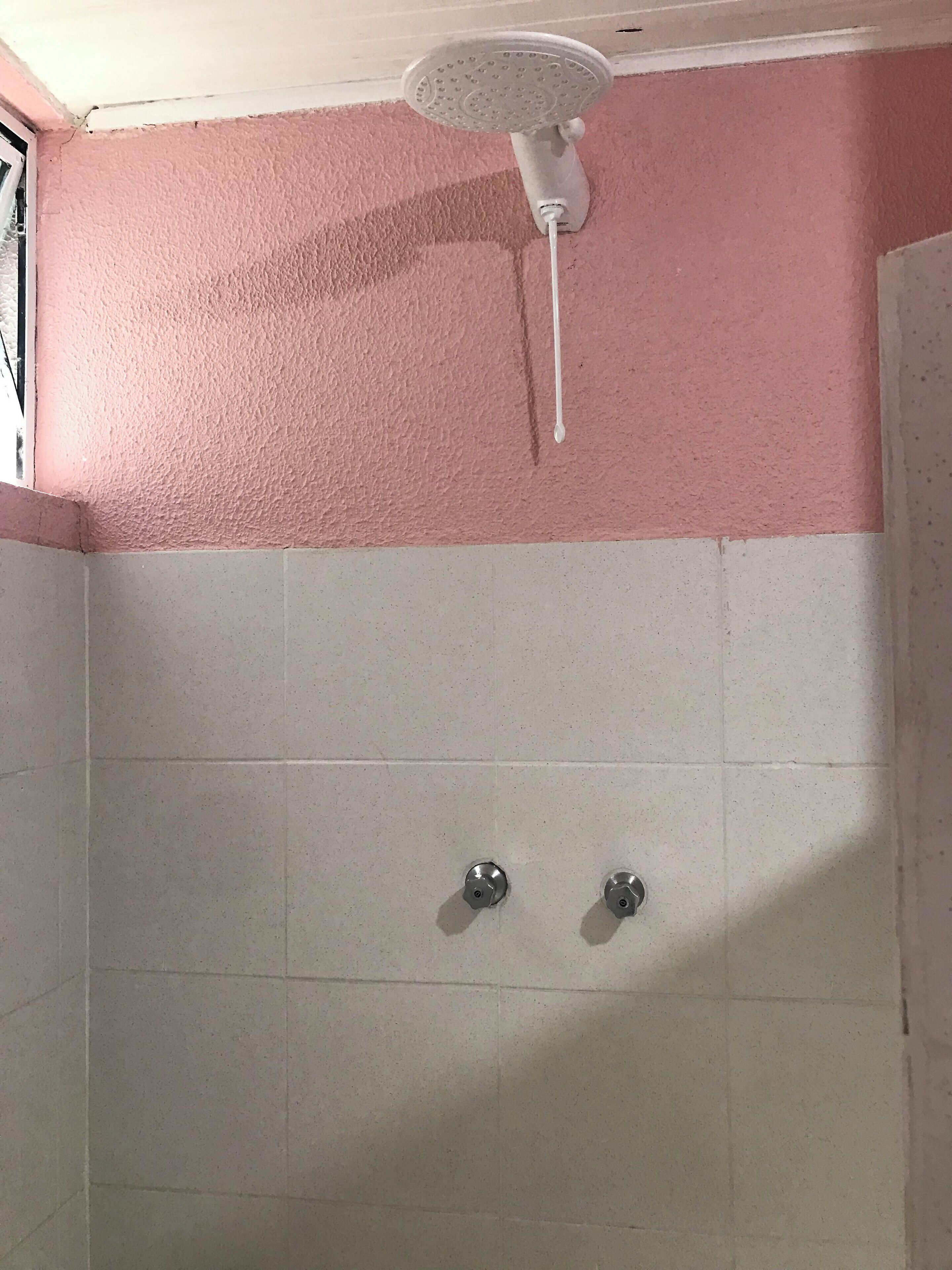 A shower area with a white ceiling fan, pink walls, and white tiled floor.