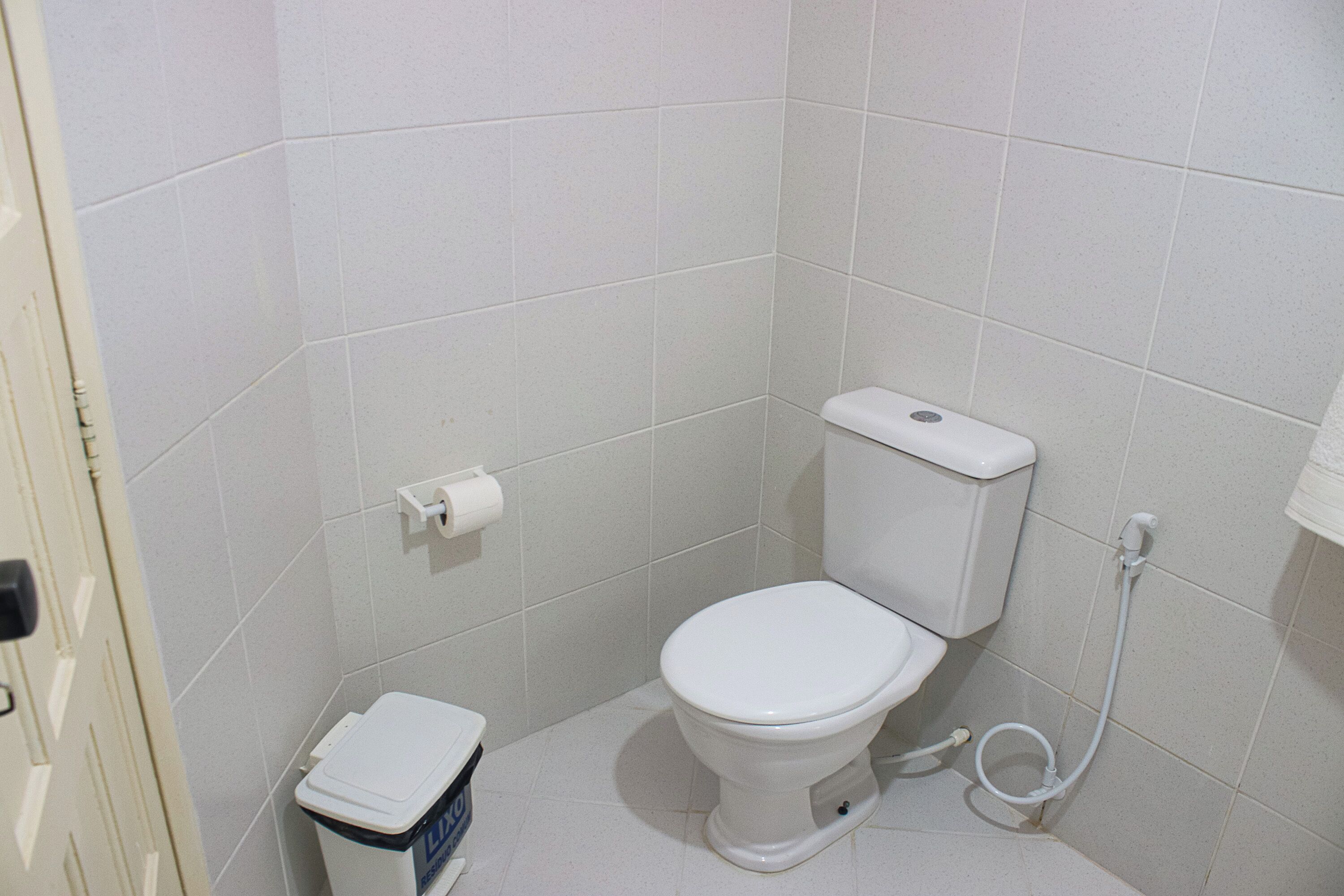 Un baño pequeño con paredes de azulejos blancos, un inodoro, un cesto de basura y un dispensador de papel higiénico.