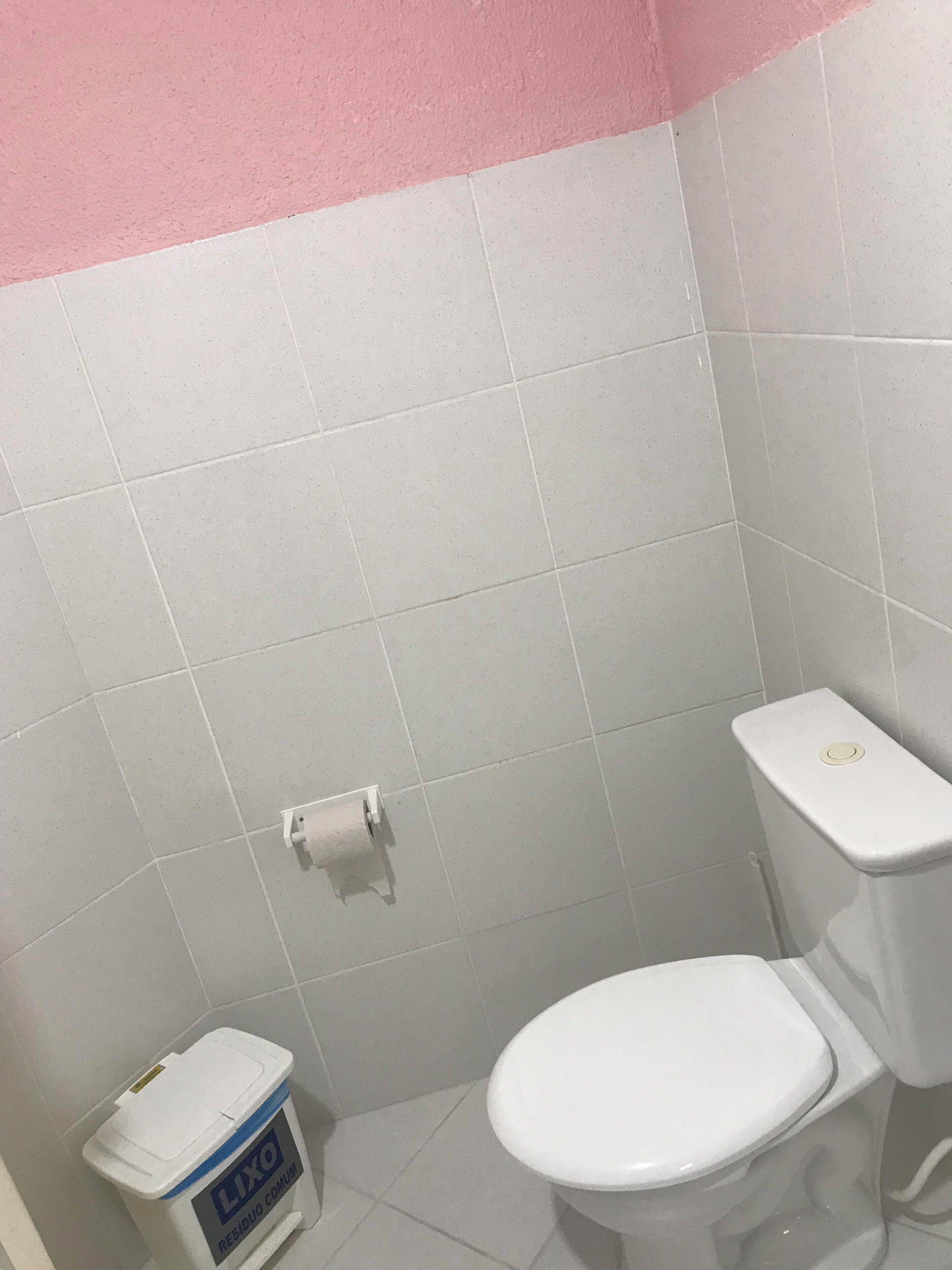 A bathroom with white tiles, a toilet, and a trash bin labeled "LIXO RESIDUO COMUM".