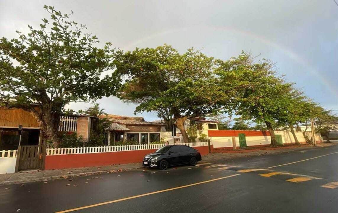 Une rue bordée d’arbres, avec une voiture garée et des maisons aux murs rouges et blancs.