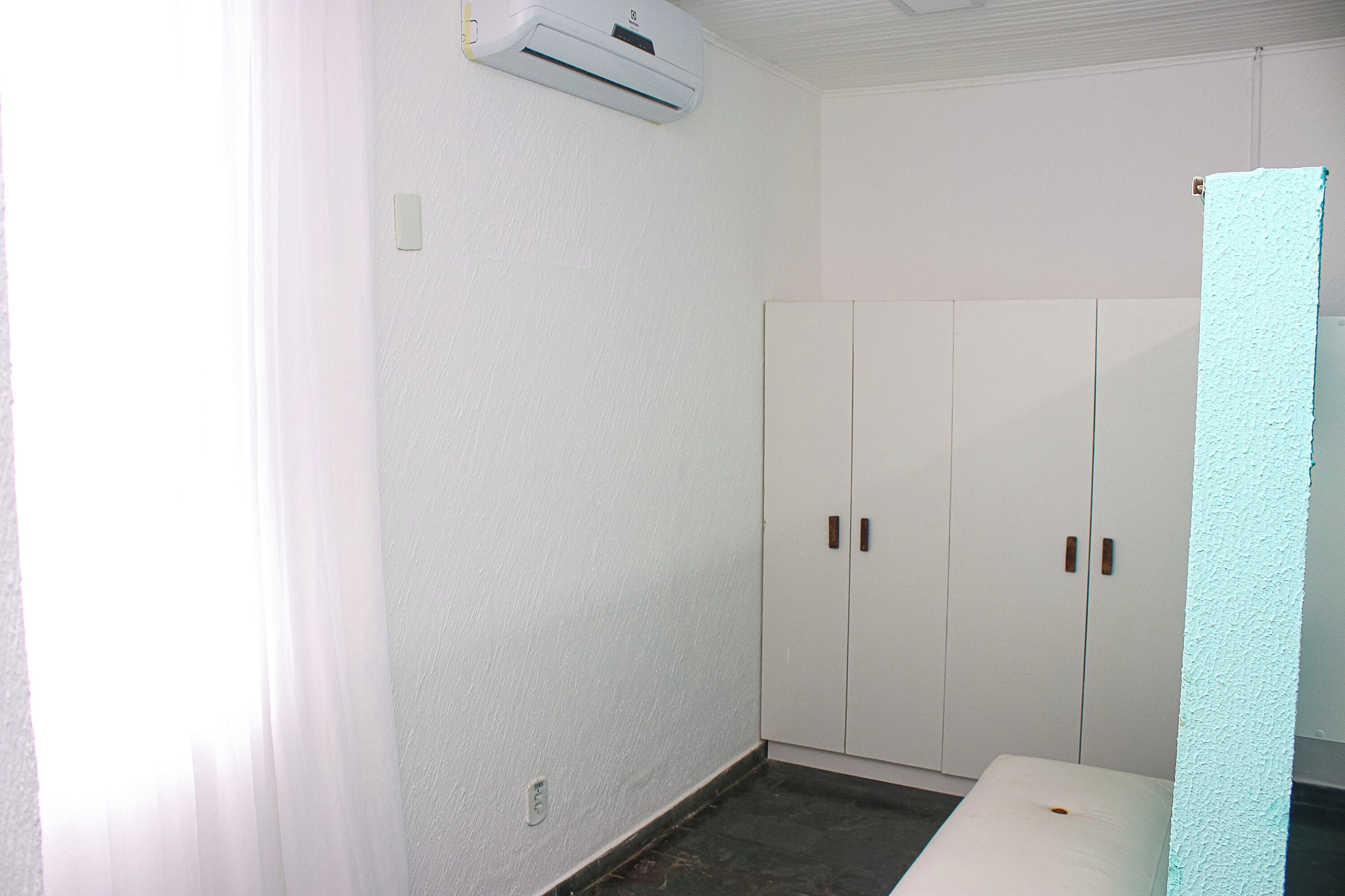 A room with a bed, a wardrobe, and an air conditioning unit on the wall.