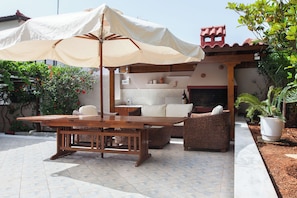 An outdoor patio with a wooden table and chairs, a large umbrella, and a small kitchen area with a tiled backsplash. - Deluxe 3 Bd House near Lagonisi w Garden (Saronikos)