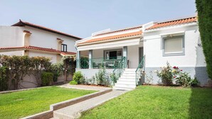 A two-story house with a covered porch, a small garden, and a staircase leading to the entrance. - Deluxe 3 Bd House near Lagonisi w Garden (Saronikos)