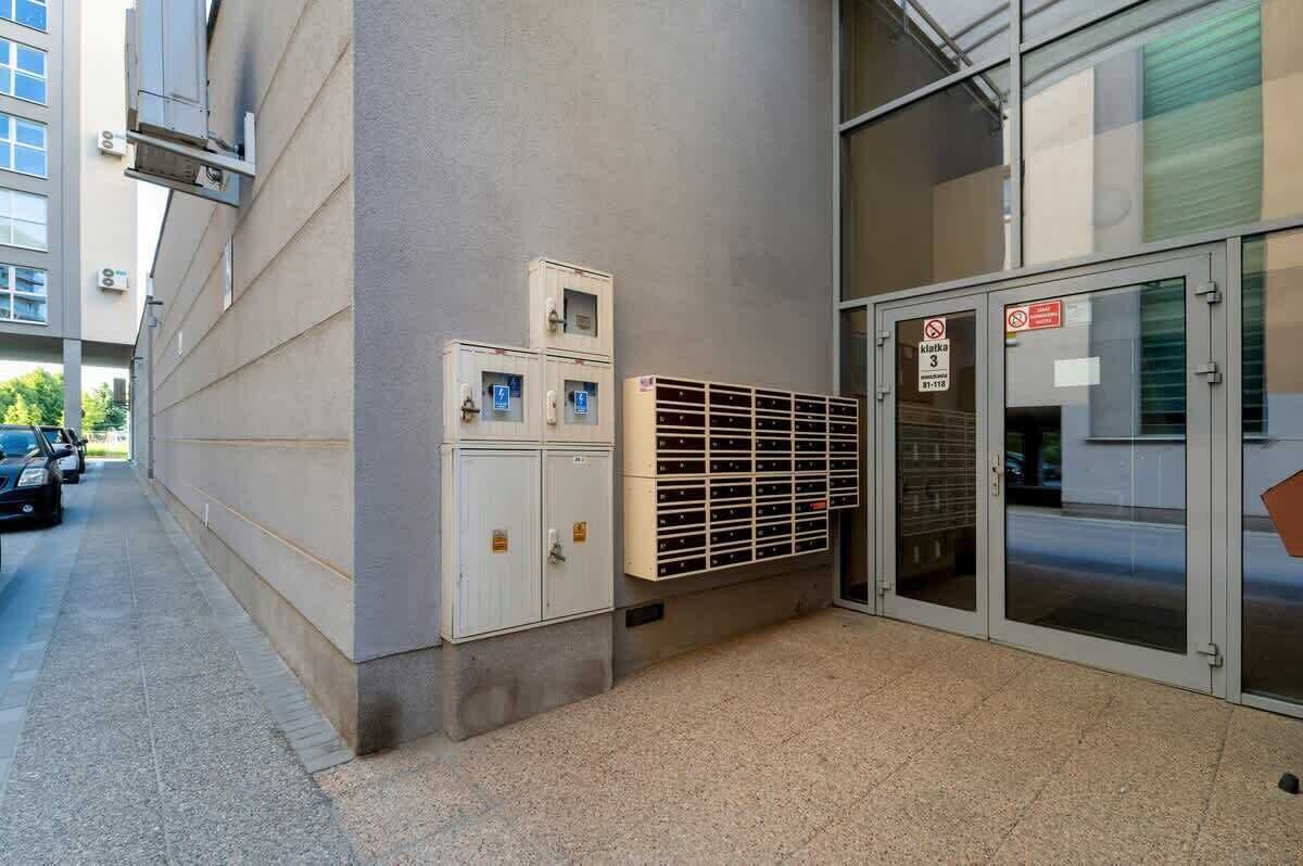 A building entrance with a fire safety sign, a metal security gate, and a row of lockers.