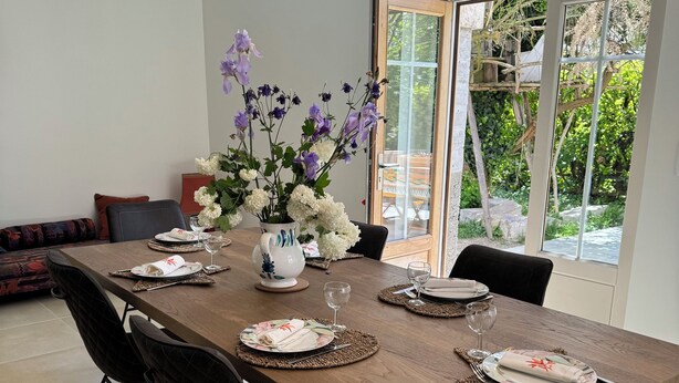 A dining area with a long wooden table set for six, black chairs, and a vase of flowers.