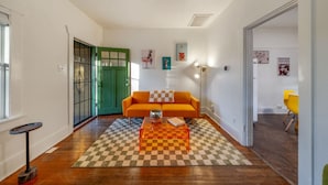 Ein Wohnzimmer mit einem Schachbrettmuster-Teppich, einer grünen Tür, einem orangefarbenen Sofa und einem Couchtisch.
