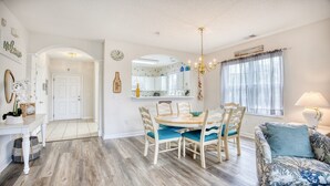 A dining area with a round table and chairs, a chandelier, and a view of the kitchen through an archway. - 1521 Ironwood - Barefoot Resort Rentals (North Myrtle Beach)