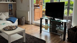 Uma sala de estar moderna com um sofá branco, uma mesa de centro com pedras decorativas, um rack de TV de vidro e uma porta de correr que dá para um jardim.