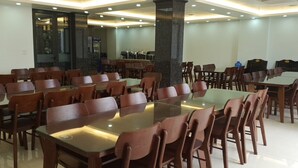 A spacious dining area with multiple tables and chairs, a large pillar, and a view of the kitchen in the background. - Bamboo Hotel (Sam Son)