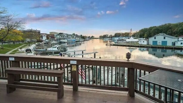 Vista para a orla marítima a partir de um deck com um banco, um cais com barcos e edifícios ao longo do rio.