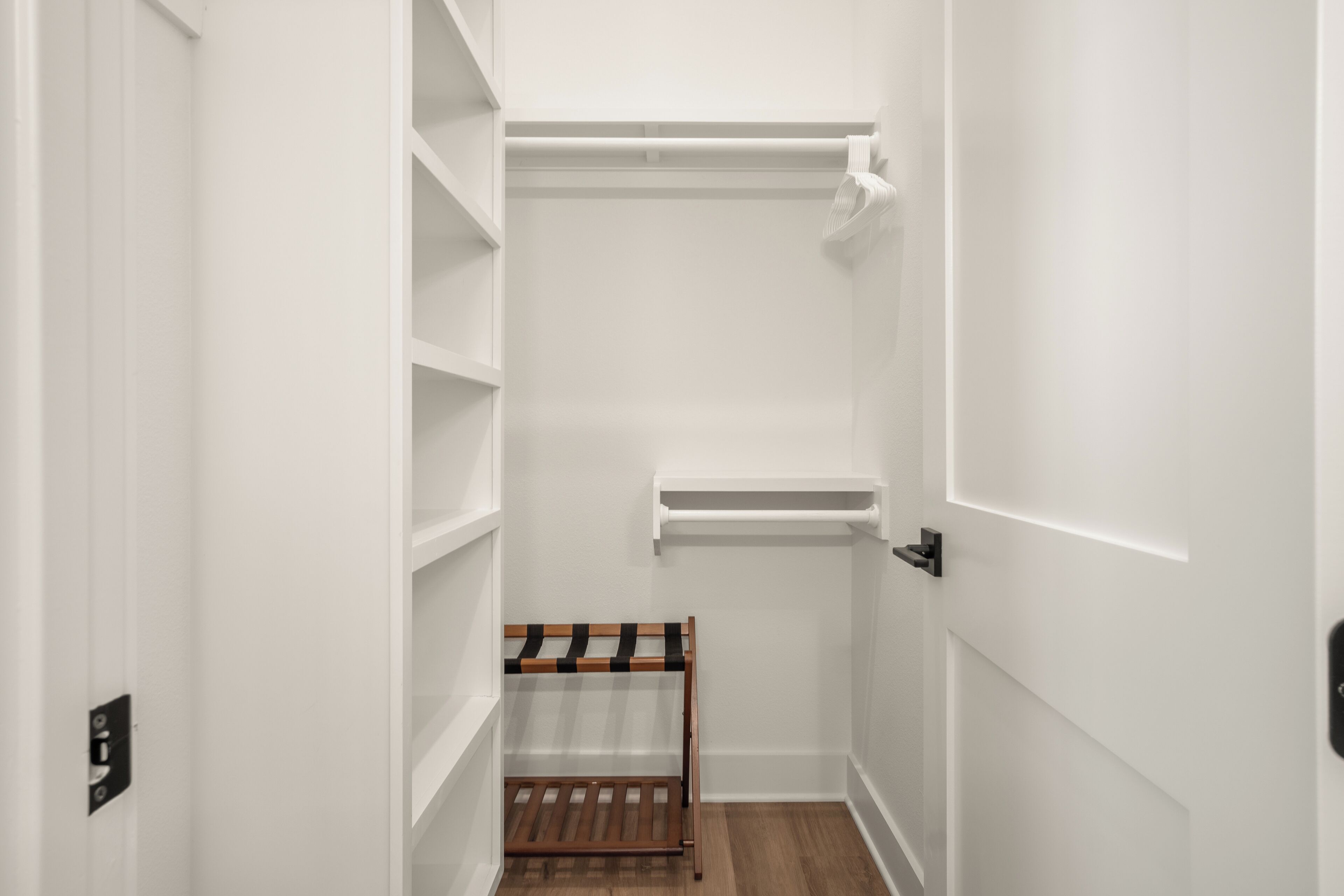 A narrow hallway with white walls, a wooden bench, and a white shelf unit.