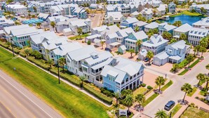 A coastal residential area with multiple-story houses, a road, and a body of water in the background. - Home w/ Bay Views, Resort Amenities & Beach Access @Cinnamon Shore North! (Port Aransas)
