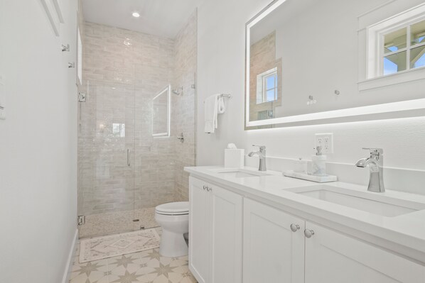 A modern bathroom with a glass-enclosed shower, a white sink with a marble countertop, and a large mirror above the sink.
