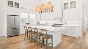 Una cocina moderna con armarios blancos, una isla grande con taburetes de bar, un refrigerador de acero inoxidable y una estufa a gas.