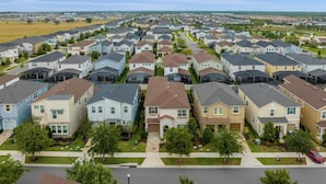 A residential neighborhood with uniform houses, well-maintained lawns, and a clear road. - Magical 7BR Disney Retreat | Pool, Spa, Game Room & Theater! (Kissimmee)