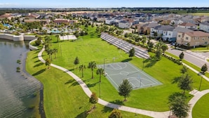An aerial view of a residential area with a basketball court, a lake, and houses. - Magical 7BR Disney Retreat | Pool, Spa, Game Room & Theater! (Kissimmee)
