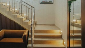 A modern staircase with glass railings and wooden steps, a framed picture on the wall, and a brown sofa in the foreground.