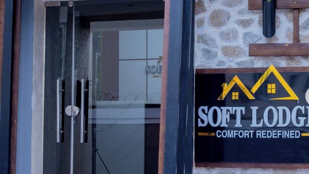A modern building entrance with a glass door, a stone wall, and a sign that reads "SOFT LODGE COMFORT REDEFINED".