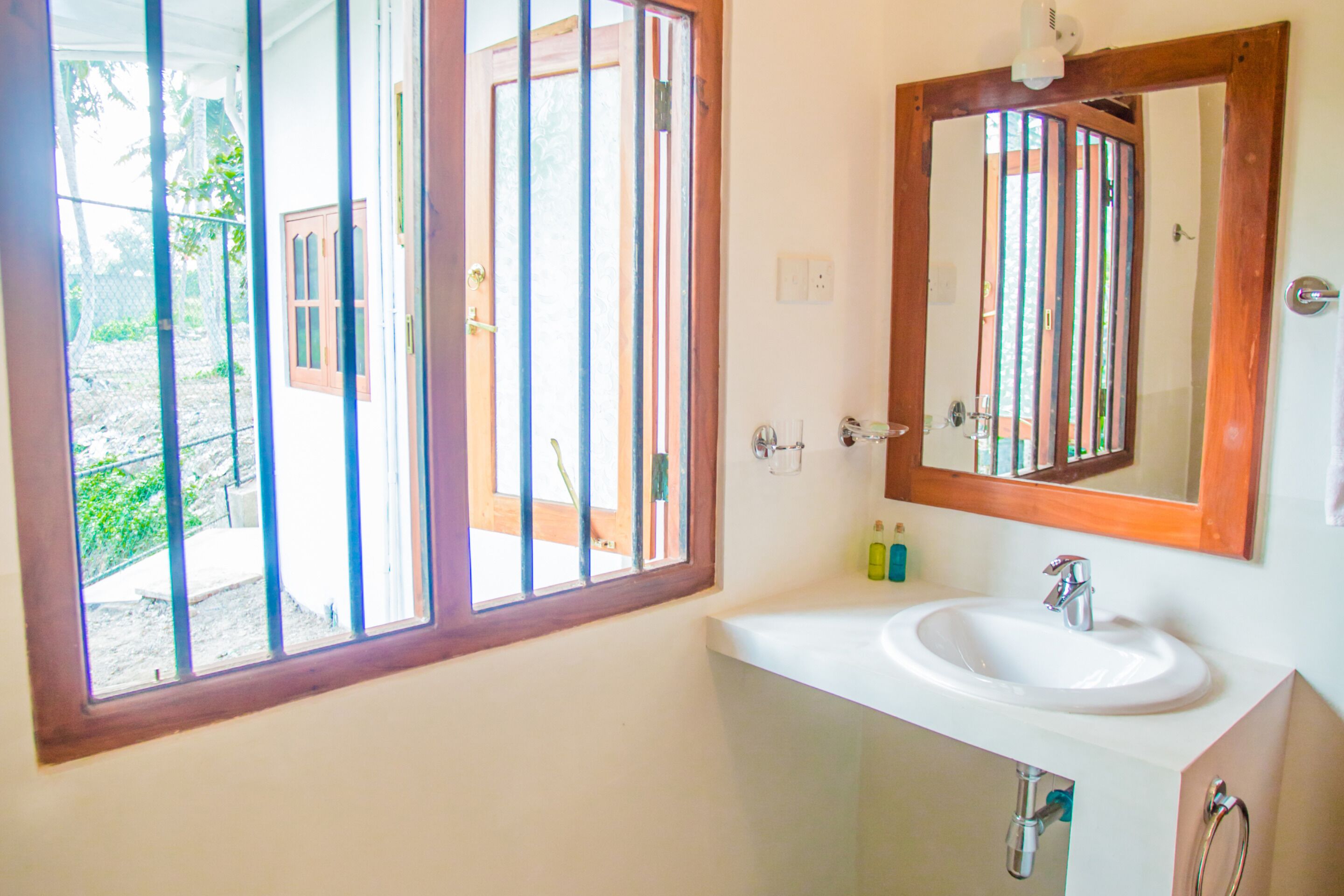 A bathroom with a window, sink, mirror, and toiletries.