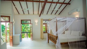 A bedroom with a wooden bed, a canopy, and a view of greenery through the windows. - South Point Surf House - Whole Villa 5 Bedrooms (Sleeps 14)  (Koggala)