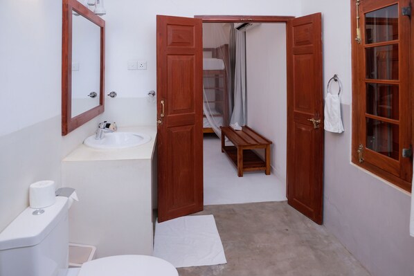 A bathroom with a wooden door, a sink, a toilet, and a shower area.