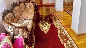 A spacious living room with a large ornate sofa, a wooden coffee table, and a chandelier. - House of Warmth (Baghdati)